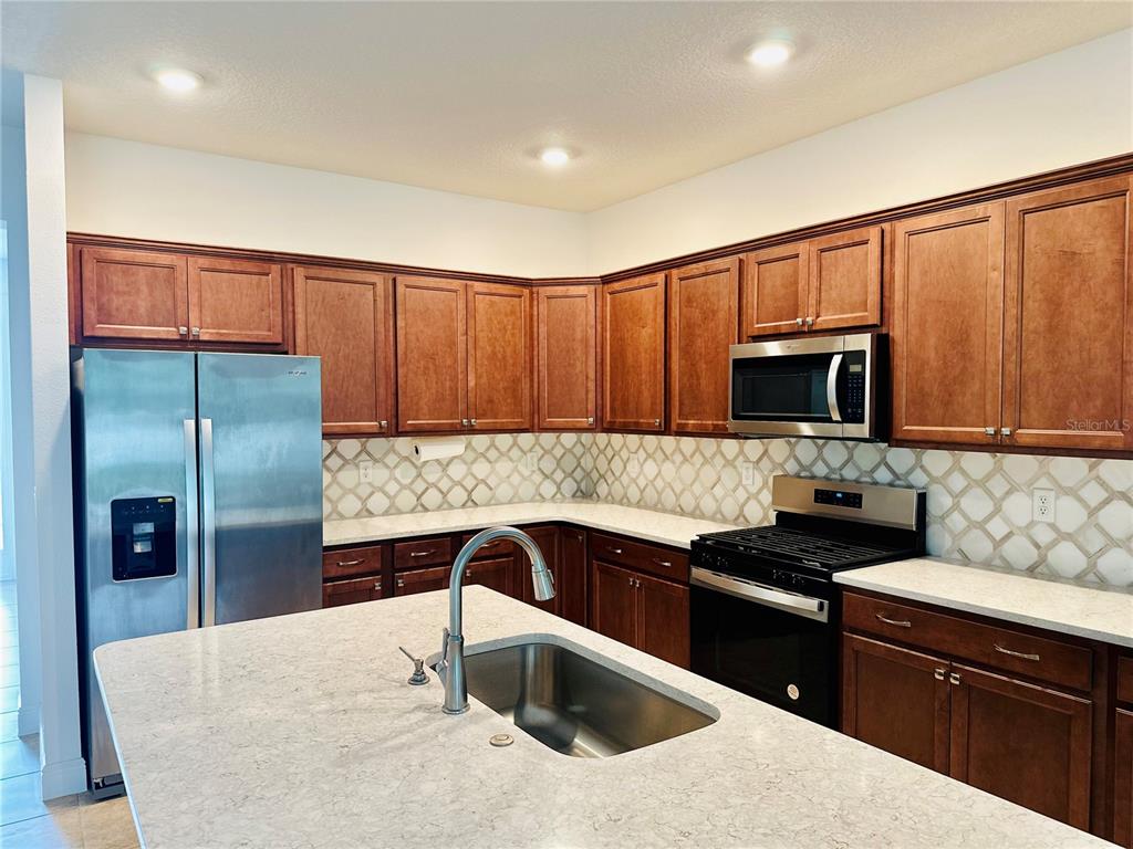 A kitchen features wood cabinets, stainless steel appliances, a center island, and a tiled backsplash — 5806 SW 78TH AVENUE ROAD, OCALA, FL