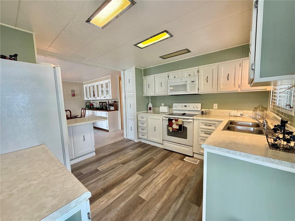 A kitchen with white cabinets, light countertops, wood-look flooring, and a view into the dining area — 117 JACARANDA DRIVE, LEESBURG, FL