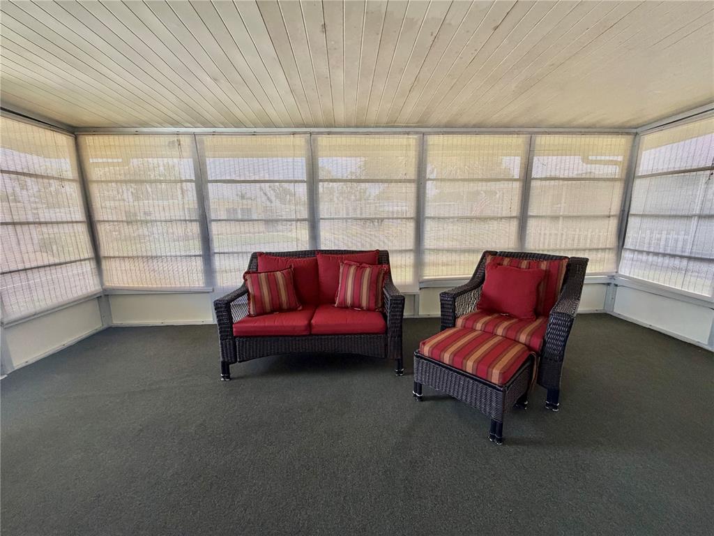 A screened-in porch features dark wicker furniture with red striped cushions and carpeted flooring — 117 JACARANDA DRIVE, LEESBURG, FL