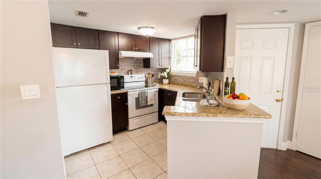 A kitchen features dark wood cabinets, granite countertops, a white refrigerator, and tile flooring — 1948 LAKE ATRIUMS CIRCLE UNIT 113, ORLANDO, FL