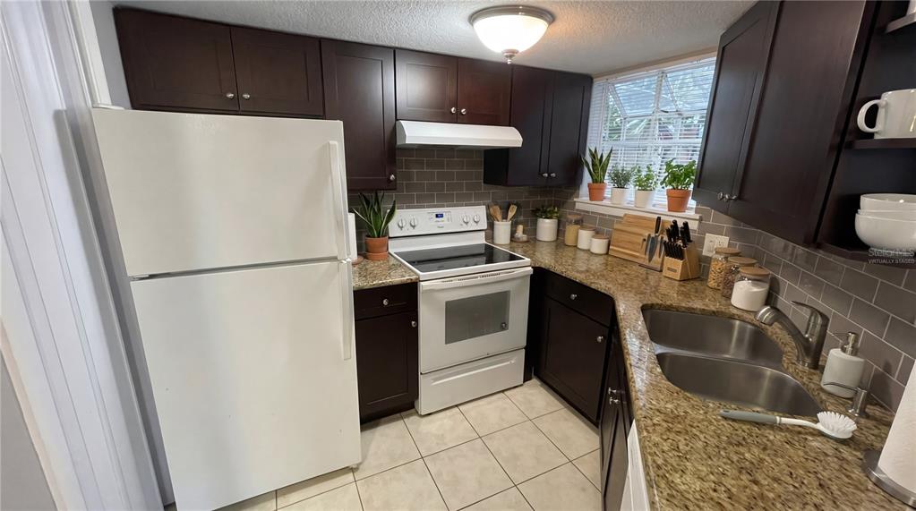 A kitchen features dark wood cabinets, granite countertops, a white stove, and a white refrigerator — 1948 LAKE ATRIUMS CIRCLE UNIT 113, ORLANDO, FL