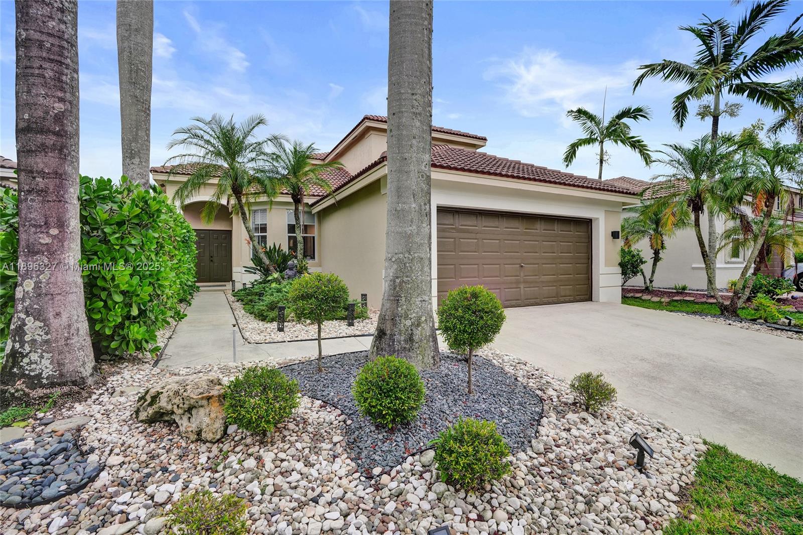 The exterior of a single-story house features a brown garage door and landscaped rock gardens — 1725 Winterberry Ln # 1725, Weston FL 33327, WESTON, FL