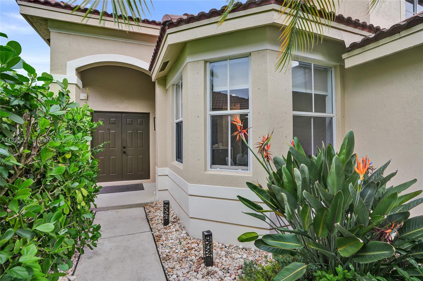 A concrete walkway leads to a double-door entrance beside a bay window and landscaping — 1725 Winterberry Ln # 1725, Weston FL 33327, WESTON, FL