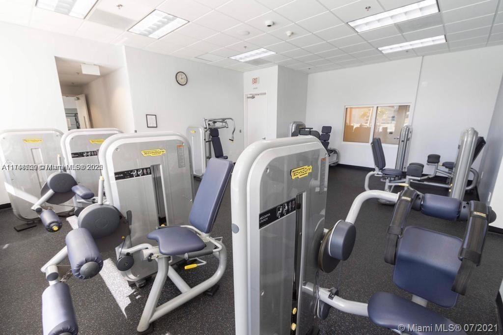 This gym features several Technogym exercise machines on a dark floor under drop ceiling tiles — 1200 Brickell Bay Dr # 3924, Miami FL 33131, MIAMI, FL