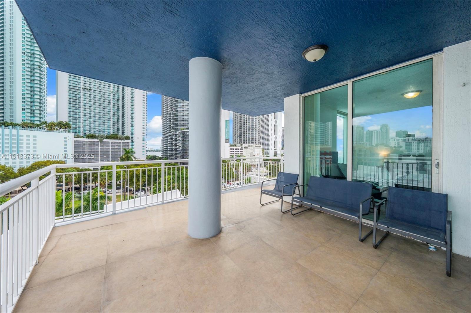 A balcony with a blue ceiling, a central support pillar, and outdoor seating overlooking city buildings — 275 NE 18th St # 708, Miami FL 33132, MIAMI, FL