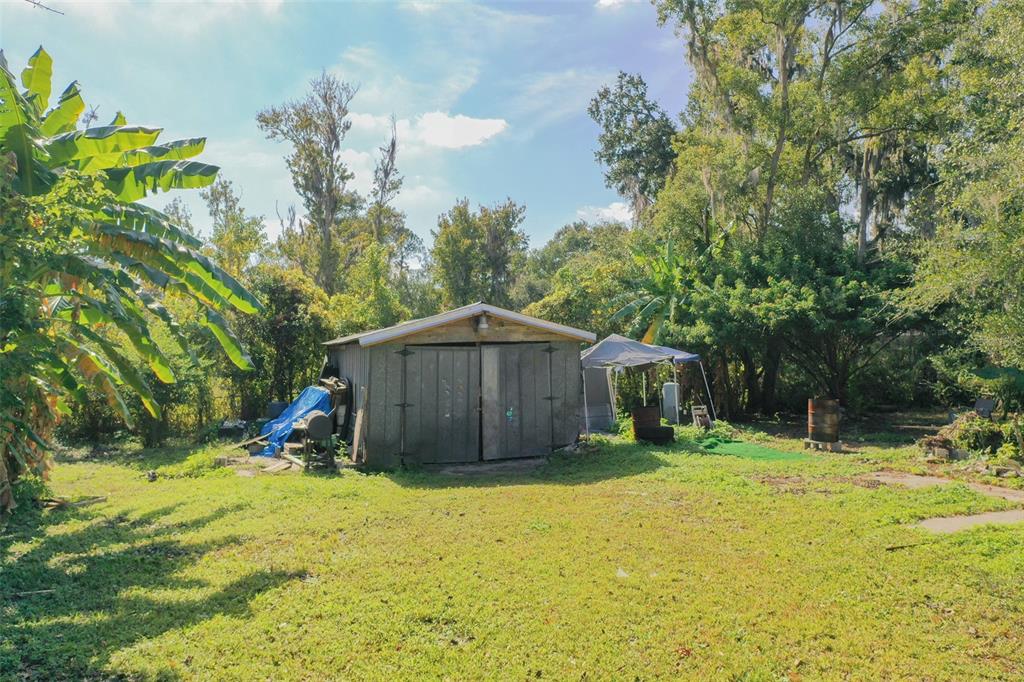 A wooden shed stands in a grassy backyard surrounded by trees and a canopy tent — 3346 STRICKLAND ROAD, LAKELAND, FL