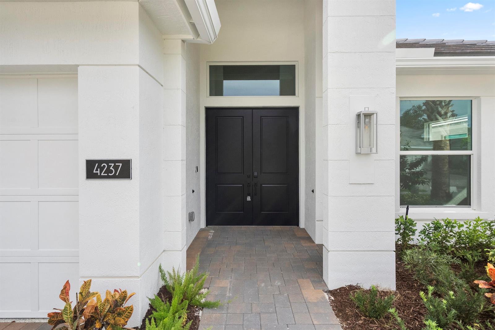 A white house exterior features a black double front door and a paved walkway — 4237 Lucaya Pointe Way, Vero Beach FL 32967, VERO BEACH, FL