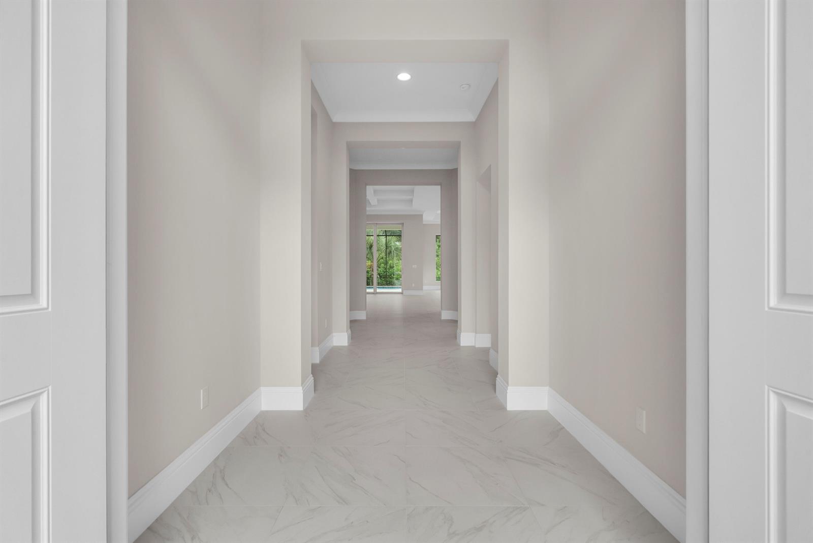 A long hallway with light-colored walls and marble-patterned tile flooring leads toward a glass door — 4237 Lucaya Pointe Way, Vero Beach FL 32967, VERO BEACH, FL