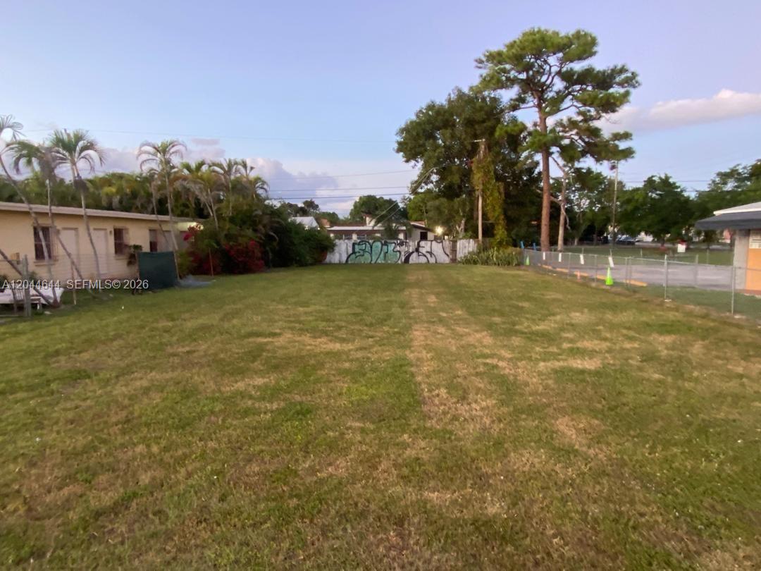 A grassy, vacant lot is enclosed by a chain-link fence with trees in the background — 3021 W Flagler St, Miami FL 33135, MIAMI, FL