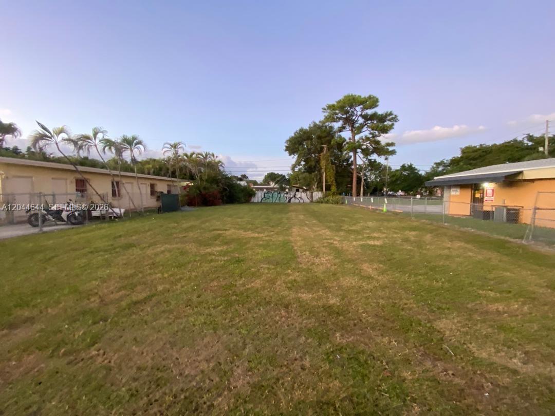 A grassy vacant lot sits between two low-rise buildings enclosed by chain-link fencing — 3021 W Flagler St, Miami FL 33135, MIAMI, FL