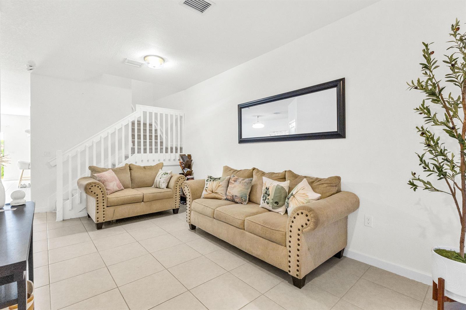 A living room features two tan sofas, a large wall mirror, and a potted tree — 2688 NW 55th Terrace, Lauderhill FL 33313, LAUDERHILL, FL