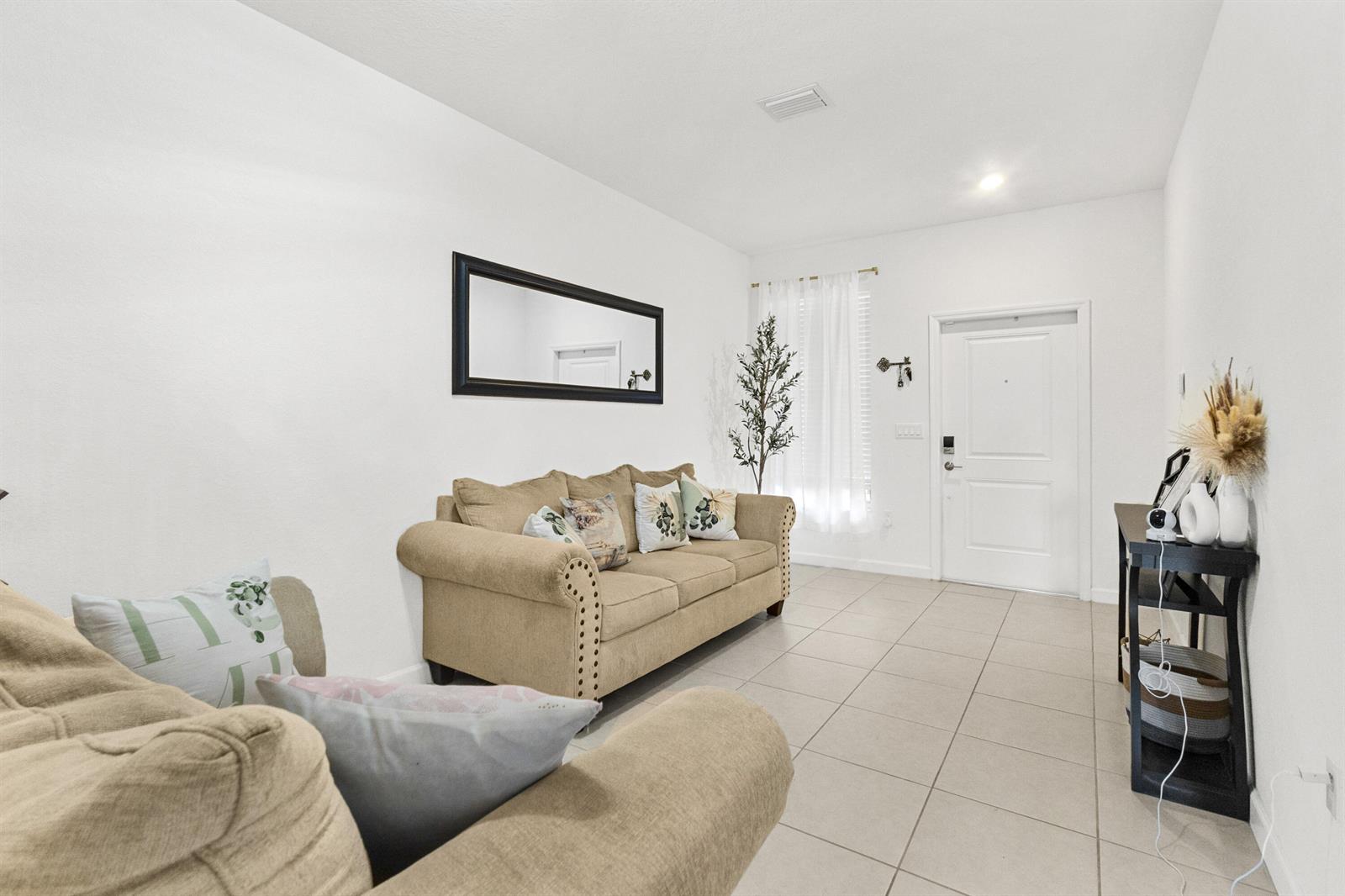 A living room features beige sofas, a black-framed mirror, and tile flooring near an entrance — 2688 NW 55th Terrace, Lauderhill FL 33313, LAUDERHILL, FL