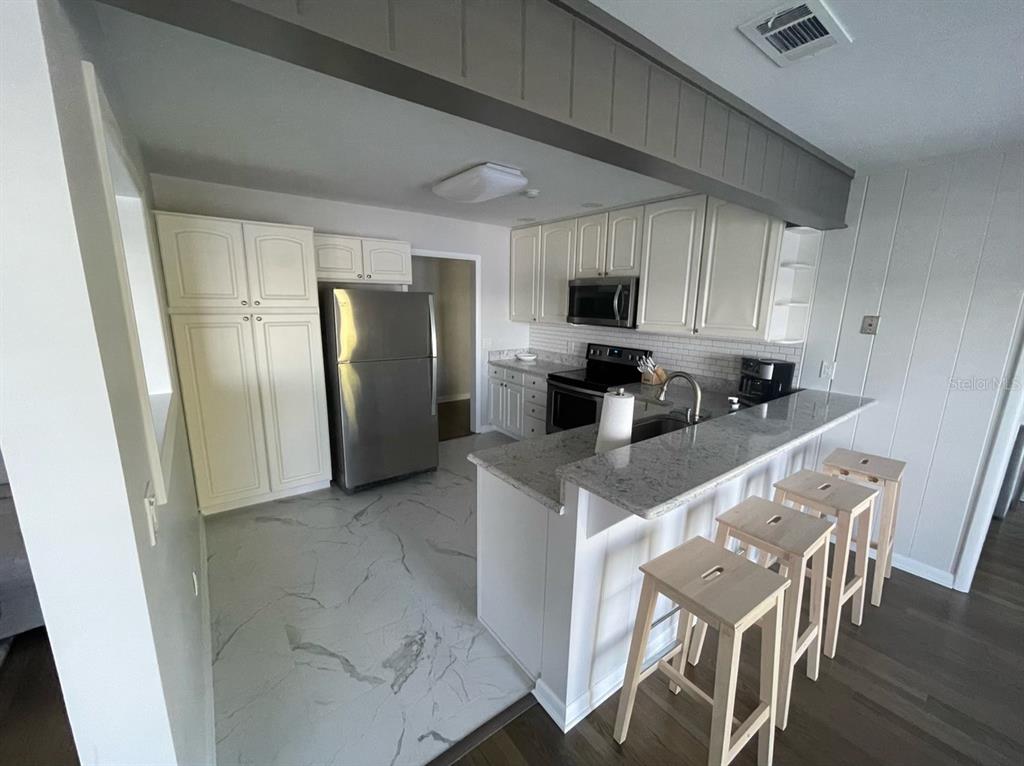 A kitchen with white cabinets, stainless steel appliances, granite countertops, and a breakfast bar — 940 N KEPLER ROAD, DELAND, FL