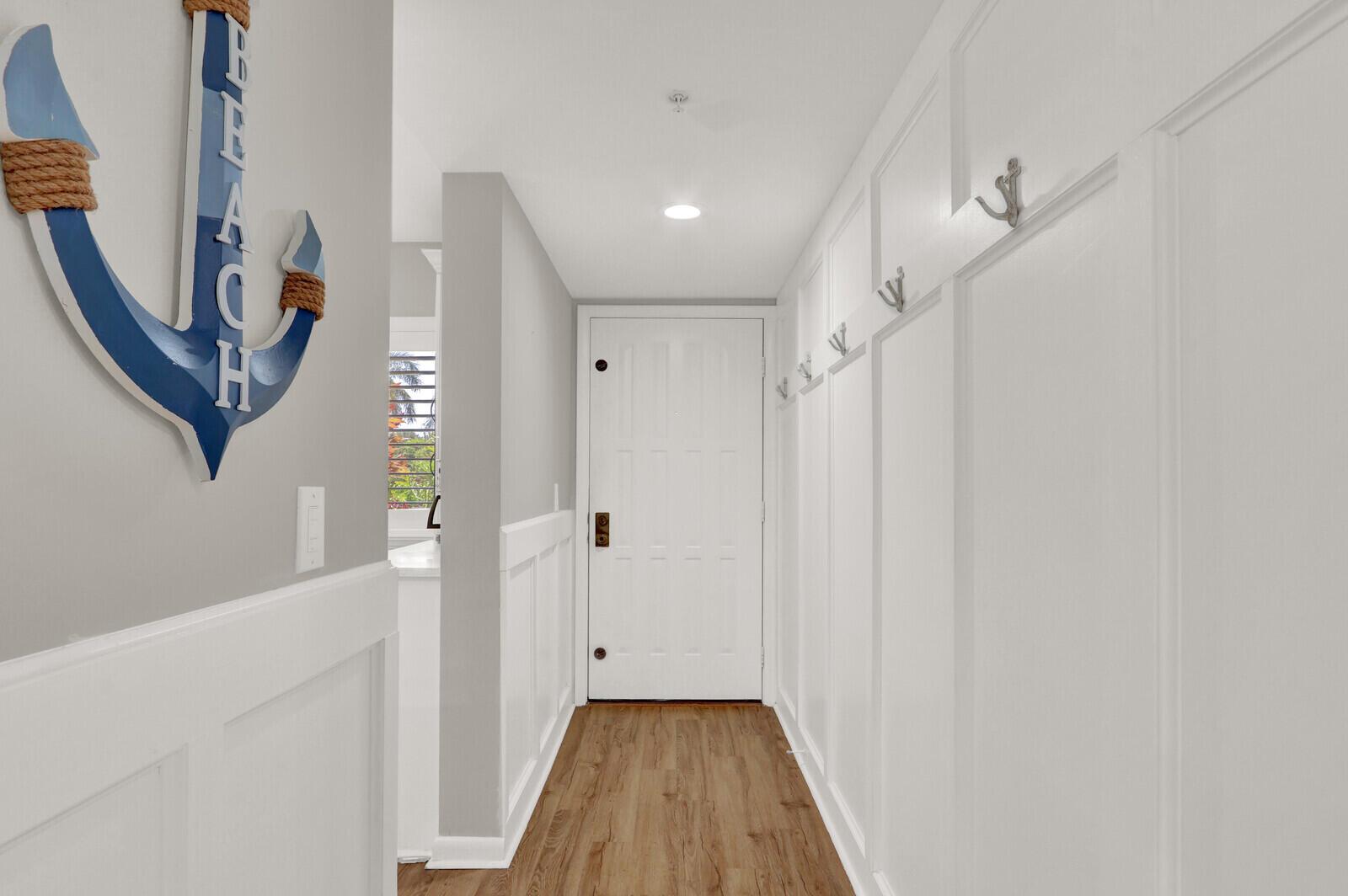 A hallway features white wainscoting, wall hooks, a decorative anchor, and a white entry door — 701 SEAFARER Circle # 105, Jupiter FL 33477, JUPITER, FL