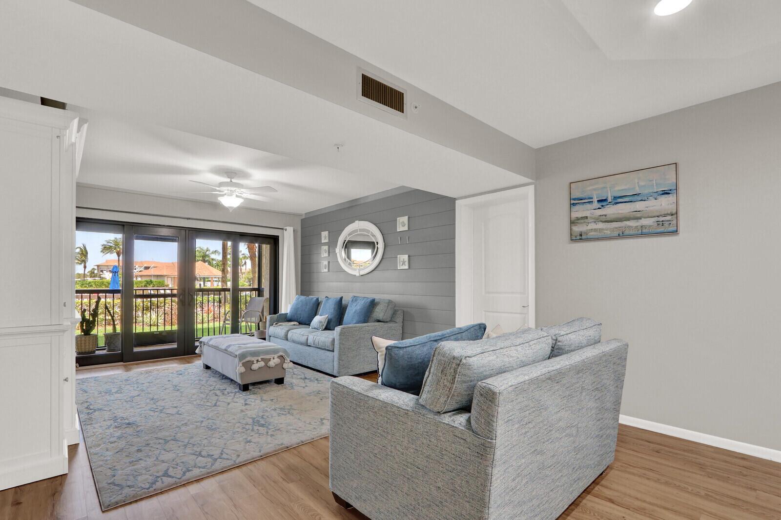 A living room features a gray shiplap accent wall, blue sofas, and a sliding glass door — 701 SEAFARER Circle # 105, Jupiter FL 33477, JUPITER, FL