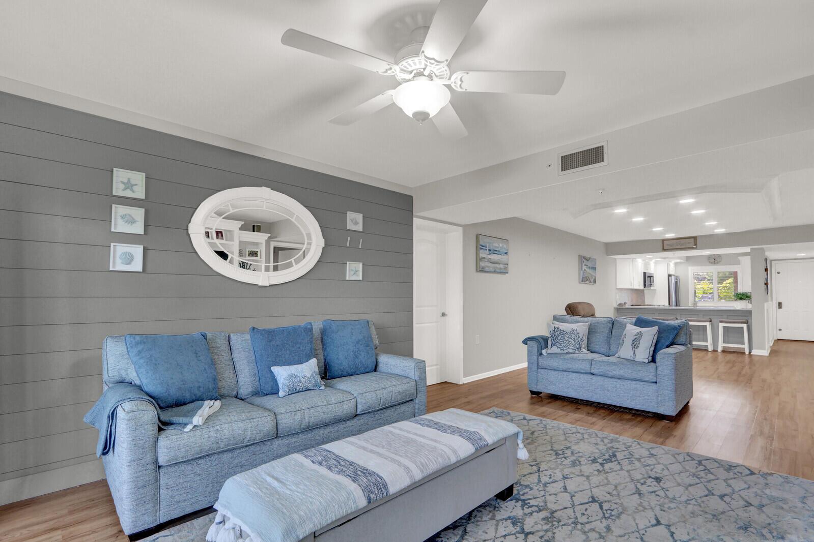 A living room with a gray shiplap wall, blue sofas, and an open kitchen area — 701 SEAFARER Circle # 105, Jupiter FL 33477, JUPITER, FL