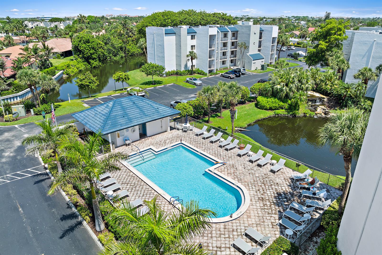 An aerial view shows a swimming pool with a blue roof cabana and surrounding pond — 1605 S Us Highway 1 # E103, Jupiter FL 33477, JUPITER, FL