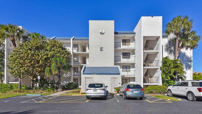 The exterior of a multi-story apartment building features a central entrance, balconies, and parking spaces — 1605 S Us Highway 1 # E103, Jupiter FL 33477, JUPITER, FL