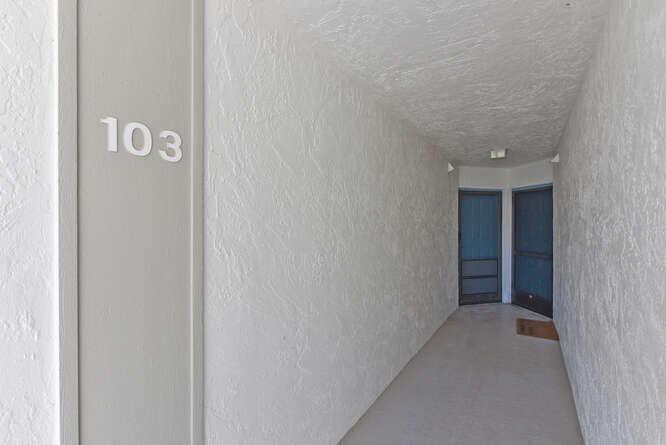 A narrow outdoor hallway features white textured walls and two dark blue screen doors — 1605 S Us Highway 1 # E103, Jupiter FL 33477, JUPITER, FL