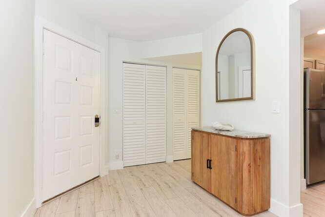 An entryway features a white door, louvered closet doors, a wooden cabinet, and an arched mirror — 1605 S Us Highway 1 # E103, Jupiter FL 33477, JUPITER, FL