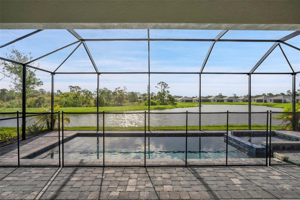 A screened-in patio features a swimming pool and spa overlooking a lake and neighborhood homes — 19100 MOSCATO COURT, VENICE, FL