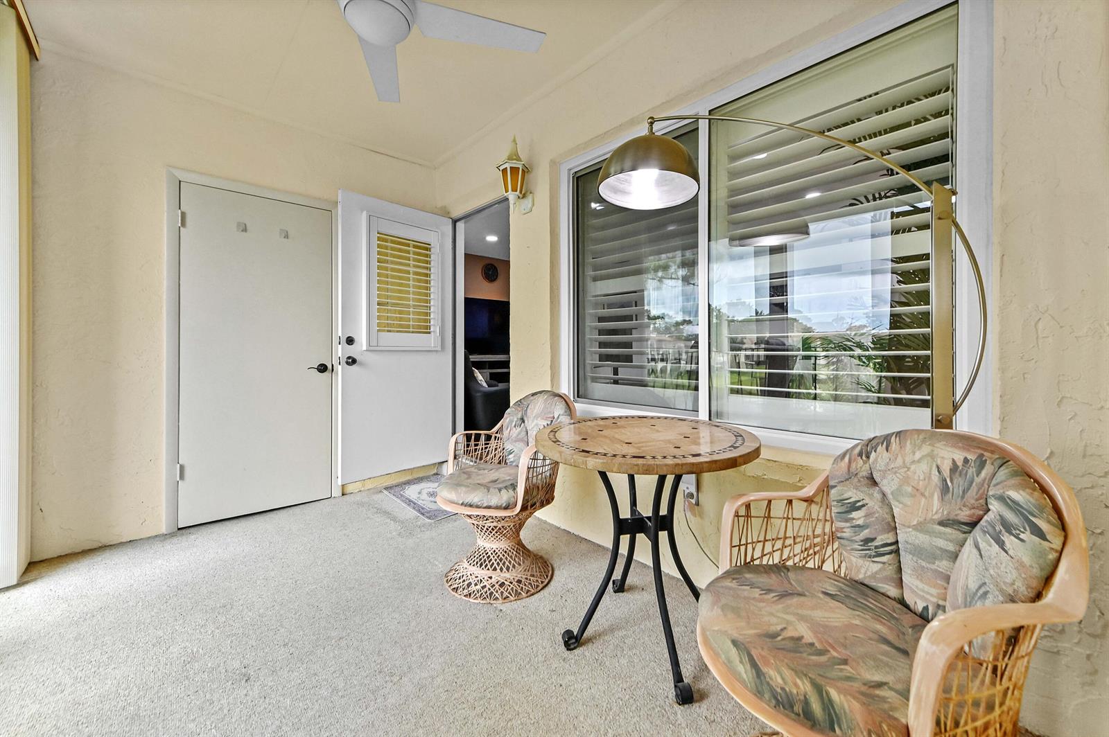 A covered patio features two wicker chairs, a small round table, and a floor lamp — 3561 Pine Tree Court # 2, FL 33463, FL