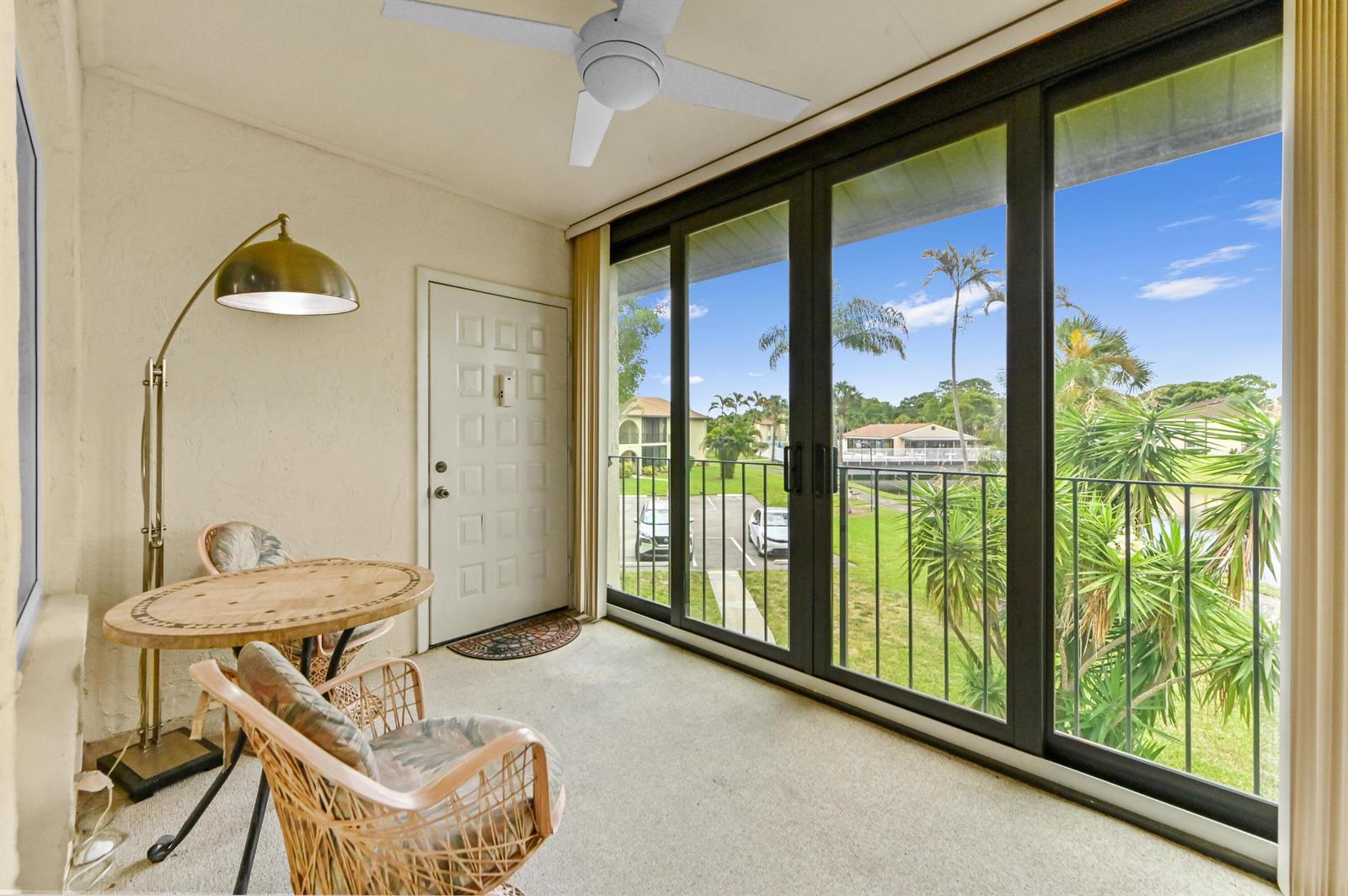 A sunroom with a table, chairs, floor lamp, and sliding glass doors overlooking a parking lot — 3561 Pine Tree Court # 2, FL 33463, FL
