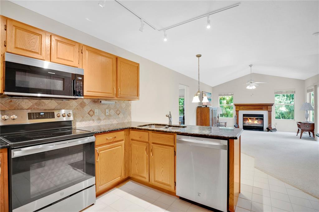 A kitchen with wood cabinets and stainless steel appliances opens to a carpeted living area — 309 OAK LEAF CIRCLE, LAKE MARY, FL
