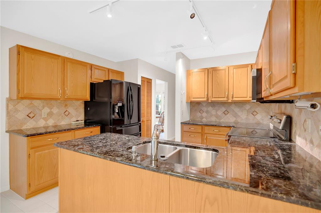 A kitchen features light wood cabinets, dark granite countertops, a central island, and black appliances — 309 OAK LEAF CIRCLE, LAKE MARY, FL
