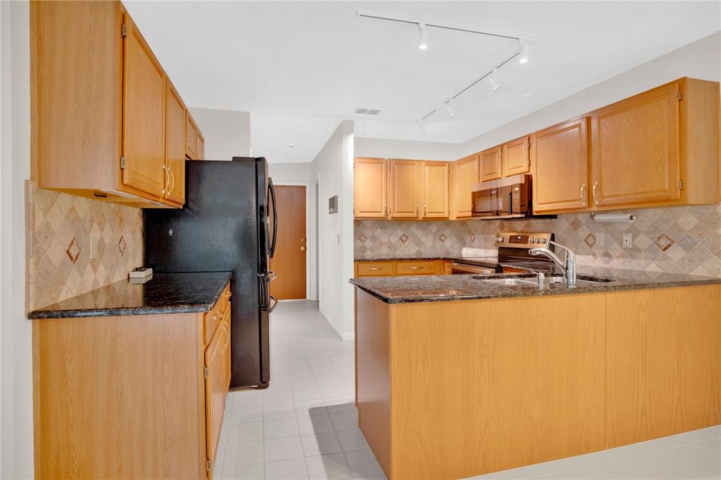 A kitchen features light wood cabinets, dark granite countertops, a black refrigerator, and tile flooring — 309 OAK LEAF CIRCLE, LAKE MARY, FL