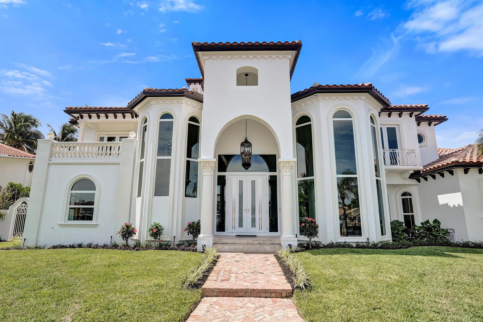 A white Mediterranean-style house features a central arched entryway, tall windows, and a tiled roof — 890 Lilac Drive, Boca Raton FL 33487, BOCA RATON, FL