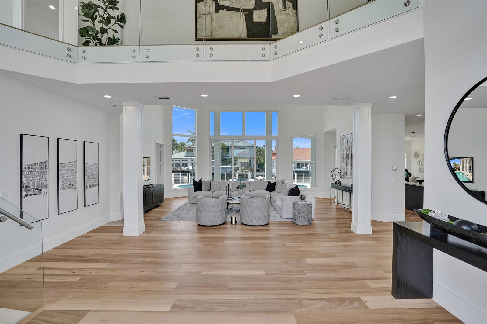 A spacious living room features light wood floors, a two-story ceiling, and large glass windows — 890 Lilac Drive, Boca Raton FL 33487, BOCA RATON, FL