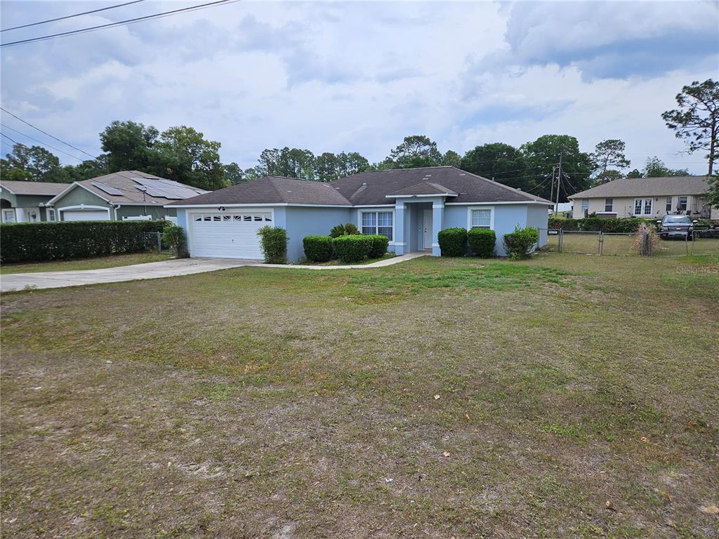A single-story light blue house with a two-car garage and a large front yard — 5704 PECAN ROAD, OCALA, FL