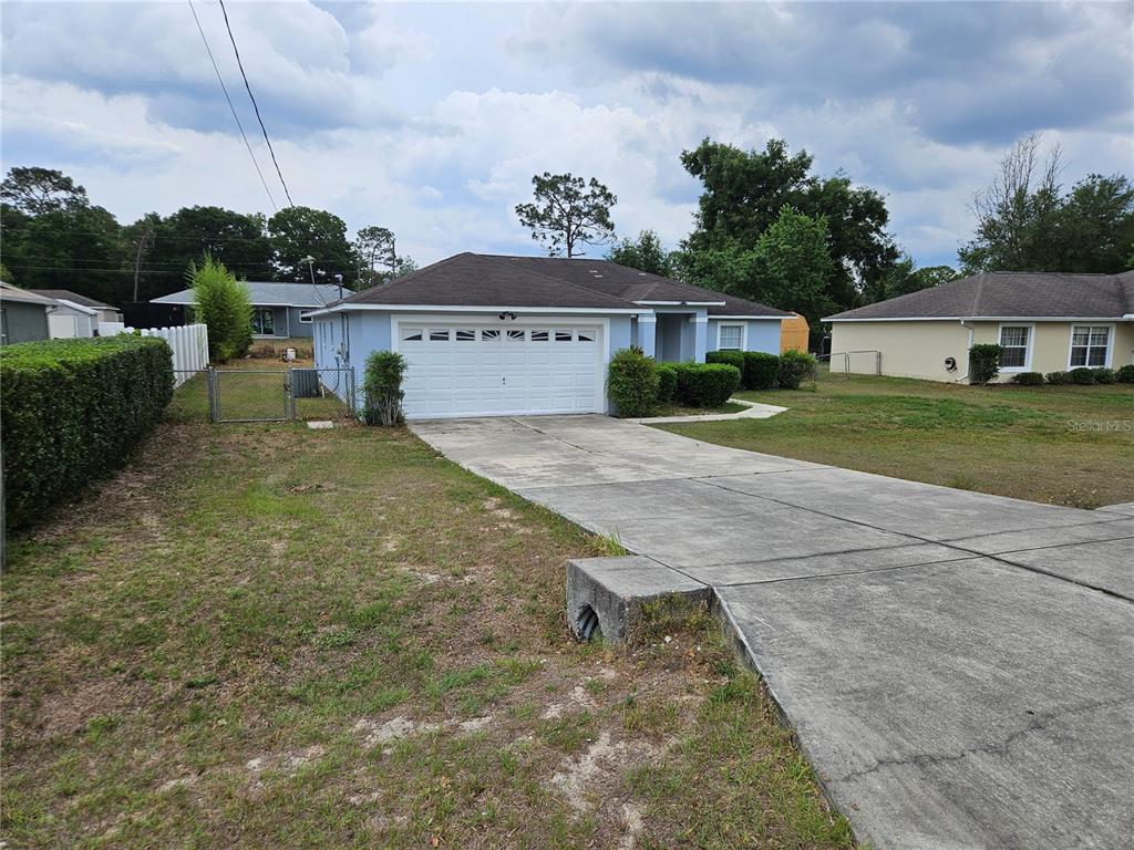 A light blue single-story house features a white garage door and a concrete driveway — 5704 PECAN ROAD, OCALA, FL