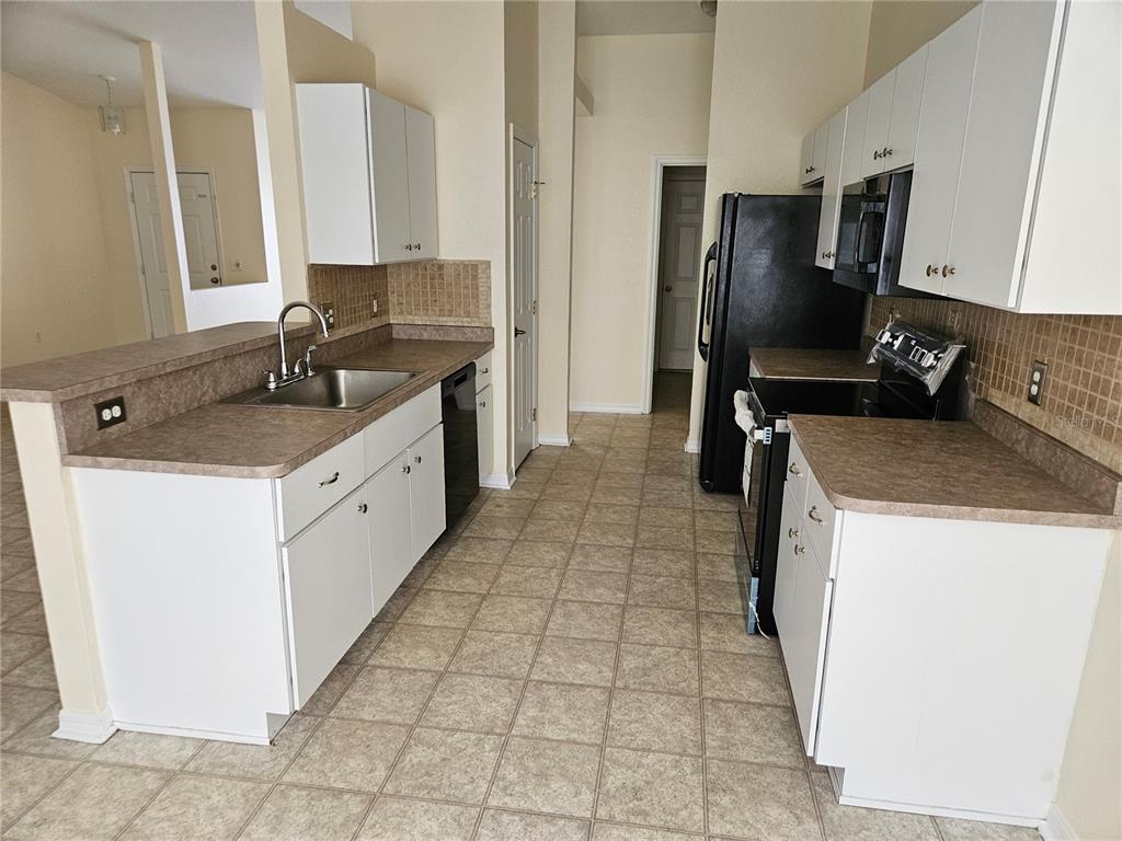 A kitchen with white cabinets, brown countertops, black appliances, and tan tile flooring — 5704 PECAN ROAD, OCALA, FL