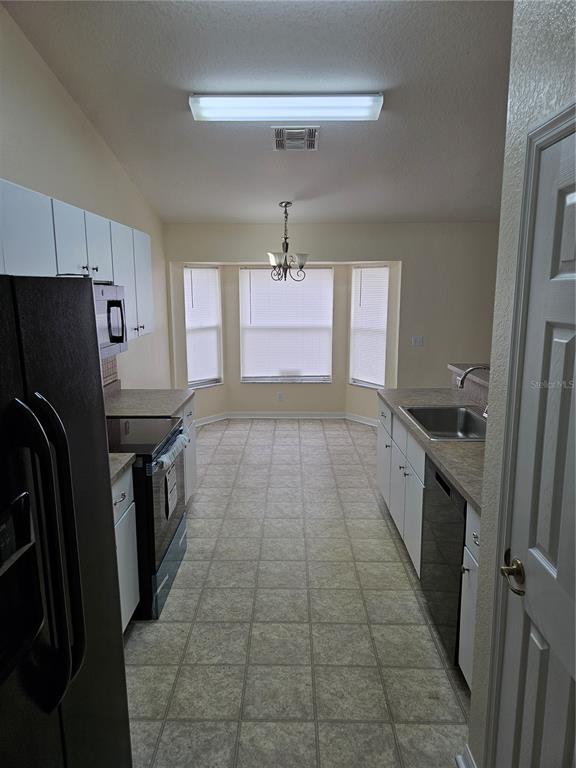 A galley kitchen features white cabinets, laminate countertops, a black appliance suite, and a dining nook — 5704 PECAN ROAD, OCALA, FL