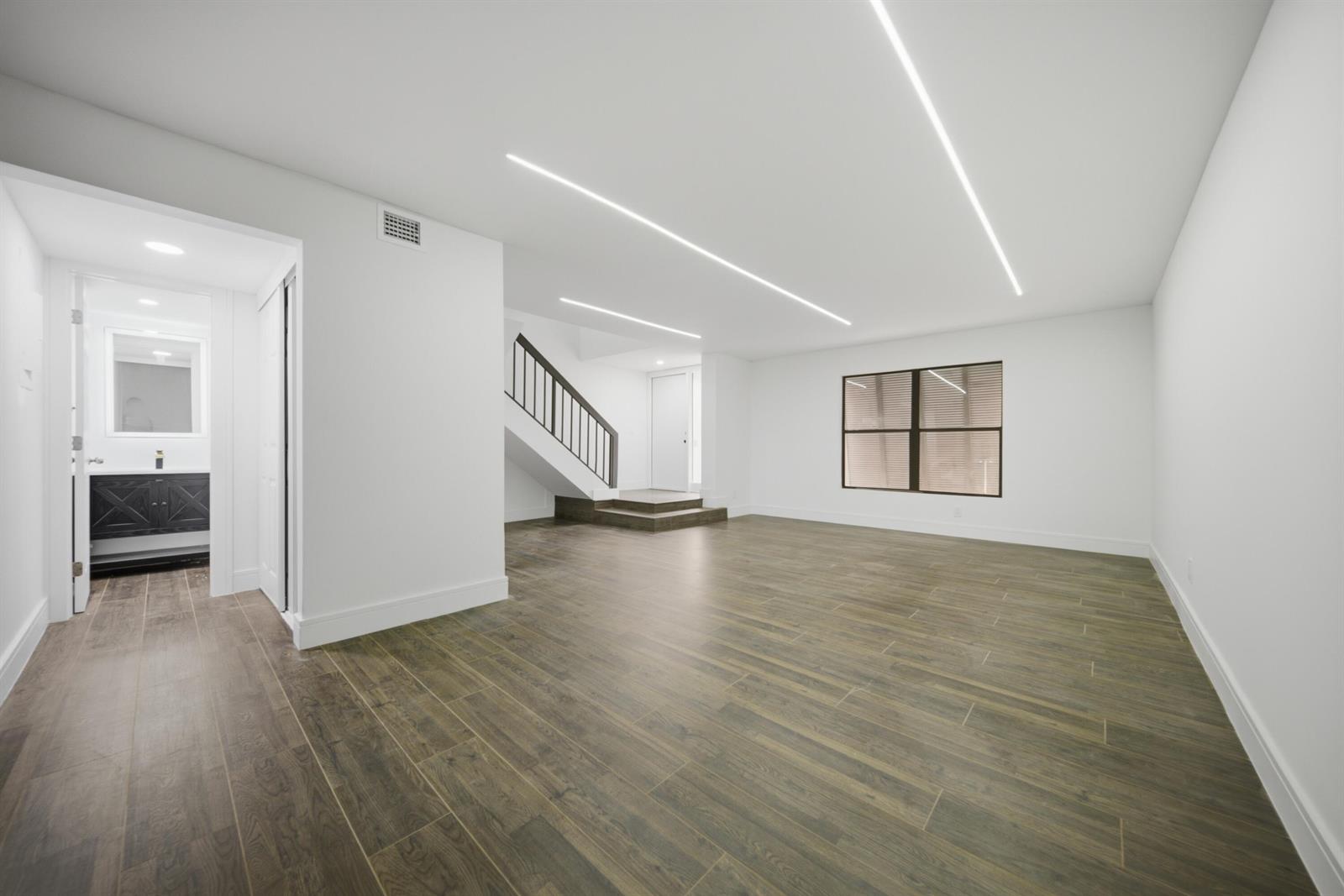 An empty room with wood-look tile flooring, recessed ceiling lighting, and a staircase — 1391 E Golfview Drive # 1391, Pembroke Pines FL 33026, PEMBROKE PINES, FL