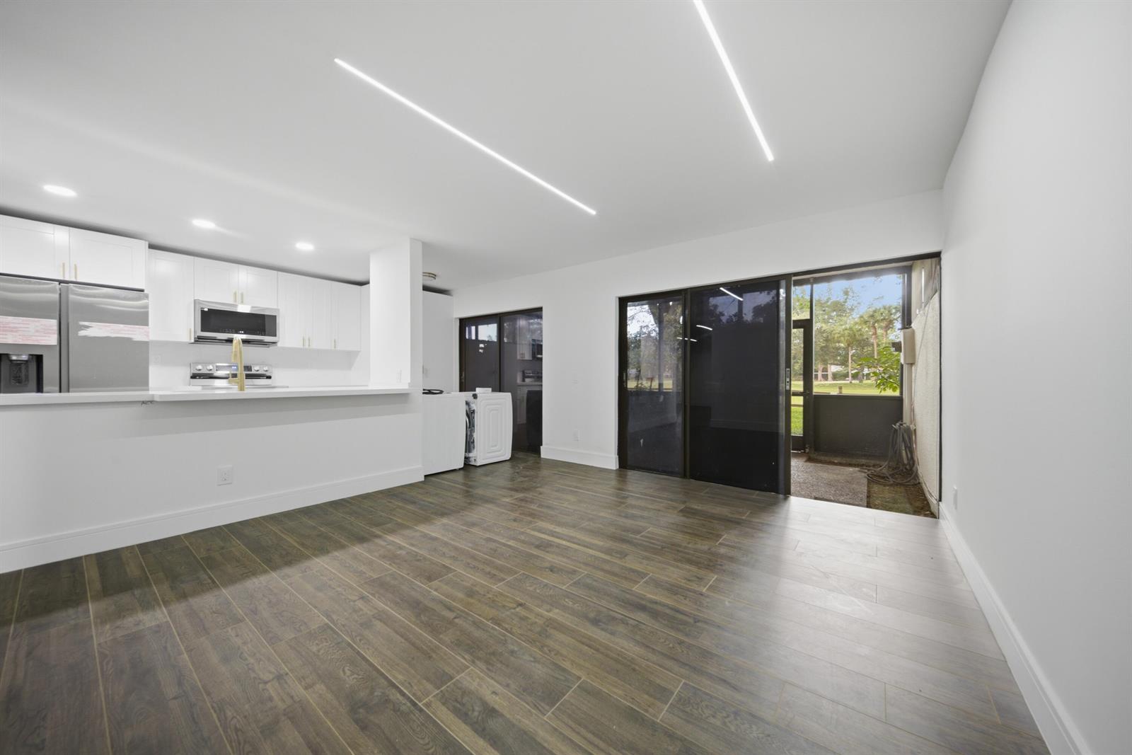 A modern kitchen and living area with white cabinets, wood-look tile floors, and sliding doors — 1391 E Golfview Drive # 1391, Pembroke Pines FL 33026, PEMBROKE PINES, FL