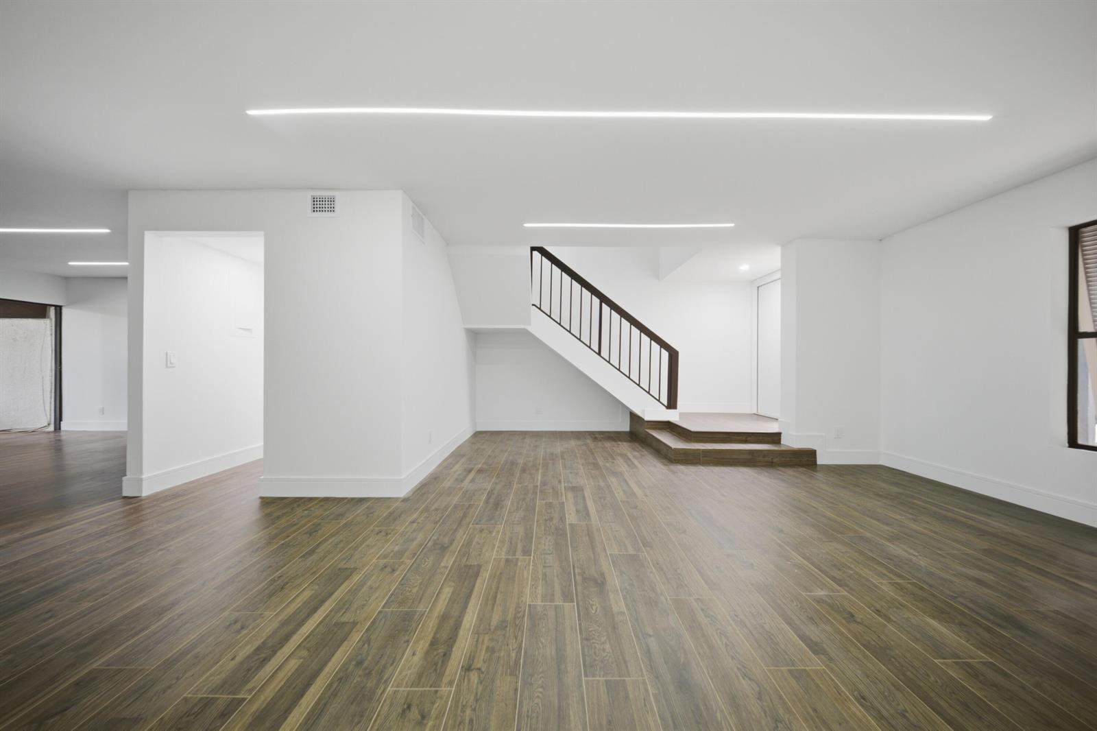 A minimalist room features white walls, wood-look tile flooring, and a staircase with dark railings — 1391 E Golfview Drive # 1391, Pembroke Pines FL 33026, PEMBROKE PINES, FL