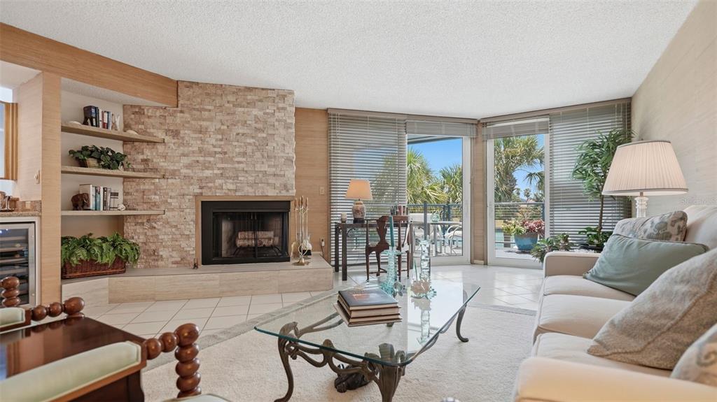 A living room features a stone fireplace, built-in shelves, tile flooring, and sliding glass doors — 910 PINELLAS BAYWAY S UNIT 201, TIERRA VERDE, FL
