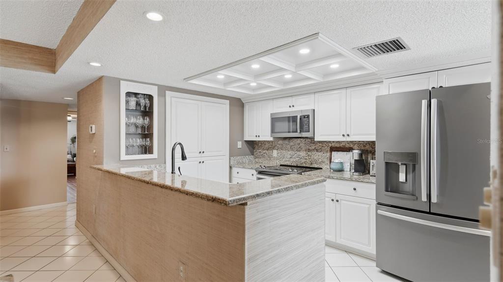 A kitchen features white cabinets, granite countertops, stainless steel appliances, and a breakfast bar — 910 PINELLAS BAYWAY S UNIT 201, TIERRA VERDE, FL