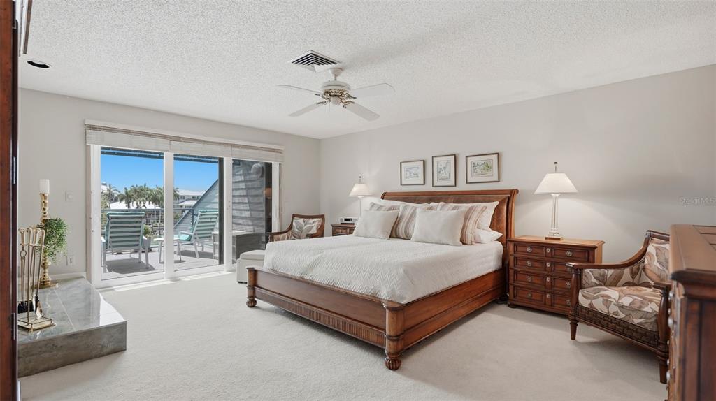 A bedroom features a wooden bed, two armchairs, a fireplace, and sliding glass balcony doors — 910 PINELLAS BAYWAY S UNIT 201, TIERRA VERDE, FL