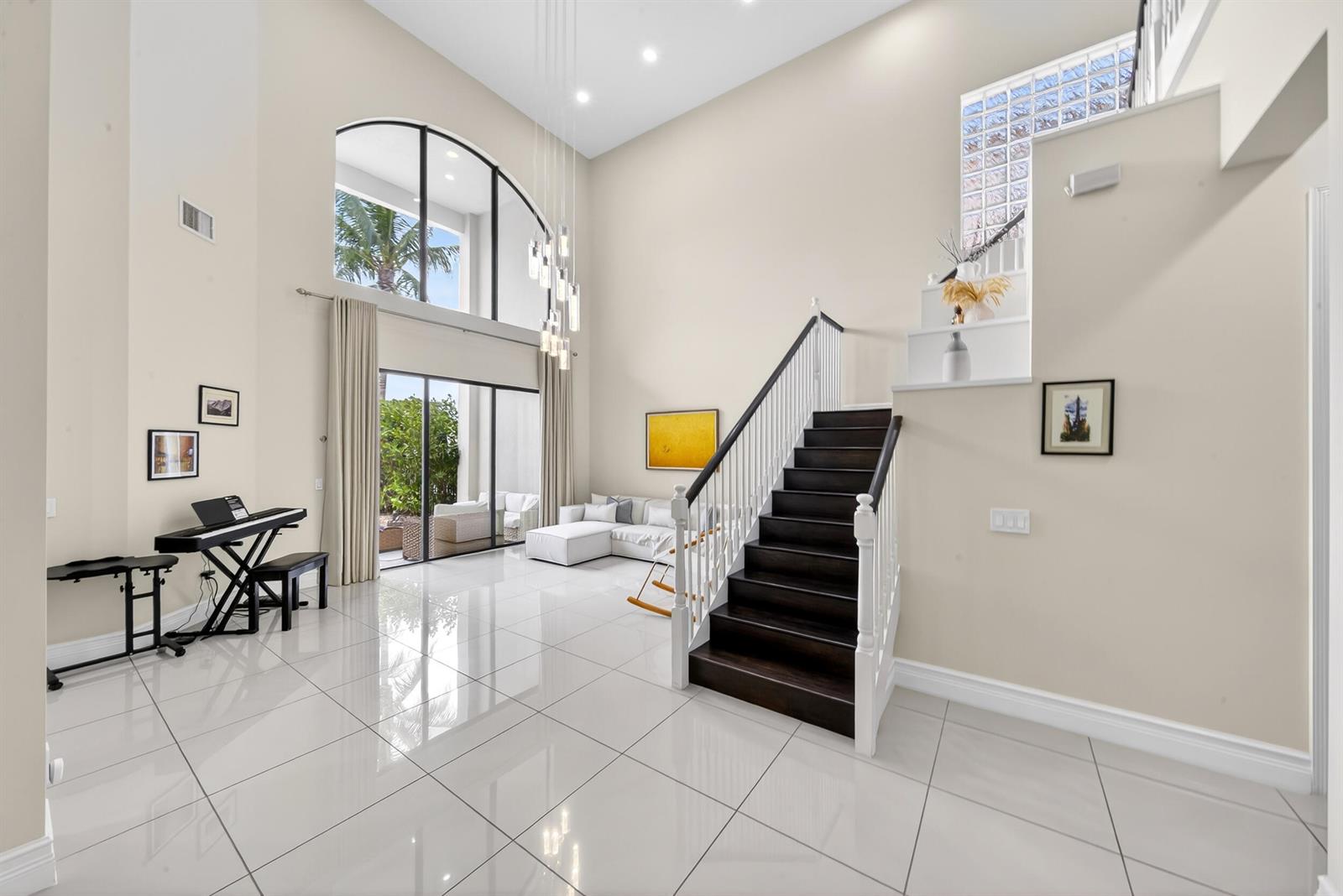 A bright living room features high ceilings, white tile floors, and a dark wood staircase — 16829 Newark Bay Road, Delray Beach FL 33446, DELRAY BEACH, FL