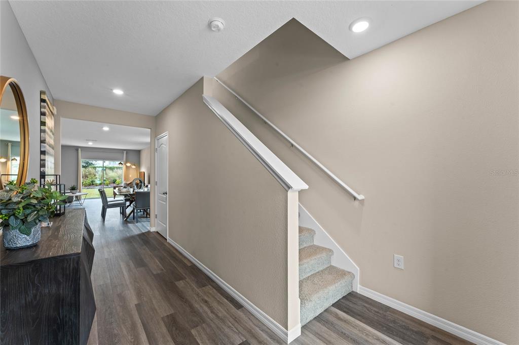 A hallway with wood-look flooring leads to a dining area past a carpeted staircase — 2121 RED ROCK ROAD, NEW SMYRNA BEACH, FL
