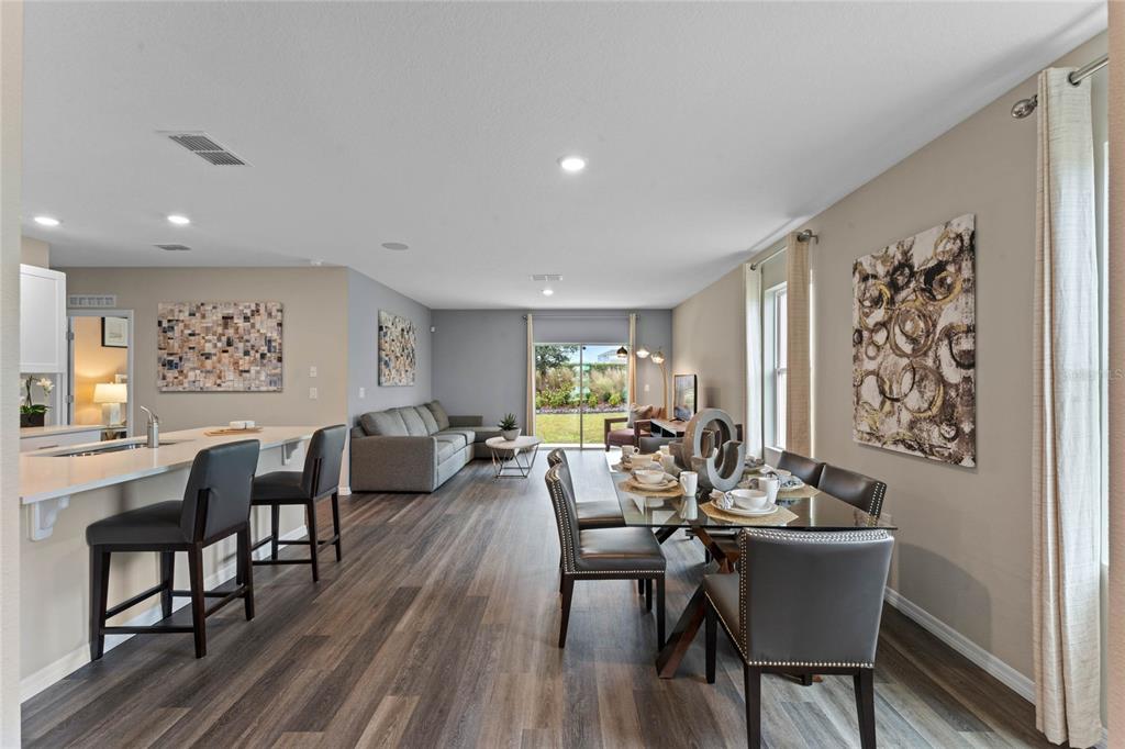 An open-concept living and dining area features wood-look flooring, a kitchen island, and sliding doors — 2121 RED ROCK ROAD, NEW SMYRNA BEACH, FL