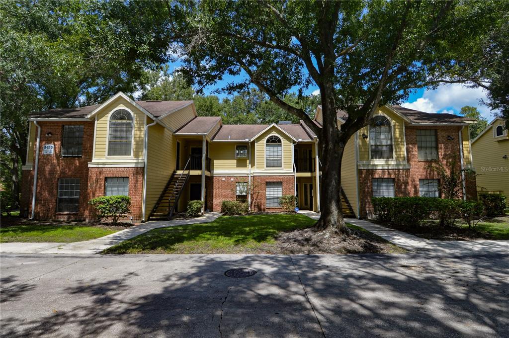A two-story apartment building with yellow siding, brick accents, and a large shade tree — 8630 MALLARD RESERVE DRIVE UNIT 103, TAMPA, FL