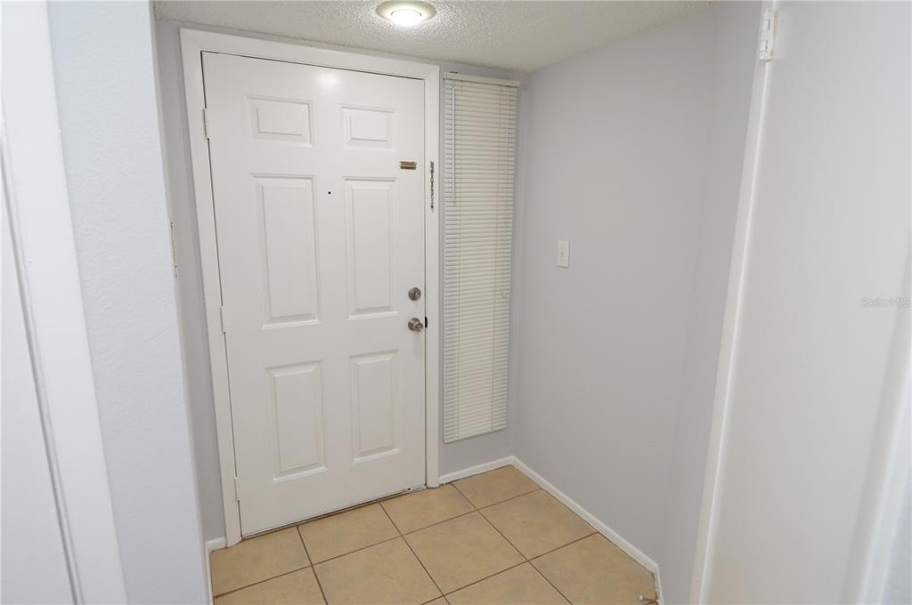 A small entryway features a white front door, light-colored walls, and tan floor tiles — 8630 MALLARD RESERVE DRIVE UNIT 103, TAMPA, FL