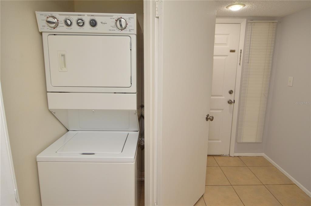 A stacked washer and dryer unit sits in a laundry closet next to an exterior door — 8630 MALLARD RESERVE DRIVE UNIT 103, TAMPA, FL