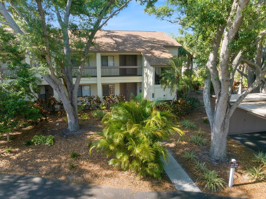 A two-story apartment building with a brown shingled roof surrounded by trees and landscaping — 772 BIRD BAY DRIVE N UNIT 104, VENICE, FL