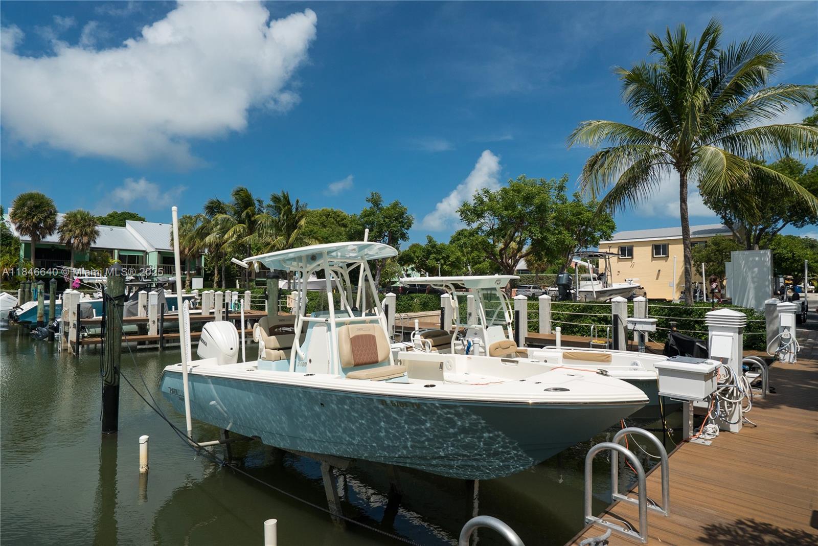A light blue center console boat is docked at a wooden pier under a blue sky — 9812 Windward Ave, Key Largo FL 33037, KEY LARGO, FL